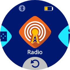Una pantalla circular muestra la casilla de Radio seleccionada en el centro de la interfaz de VEX AIM. La casilla tiene un icono de antena blanca con ondas de señal sobre un diamante naranja y la etiqueta "Radio" debajo. En la esquina superior derecha se muestra un icono amarillo de batería baja.