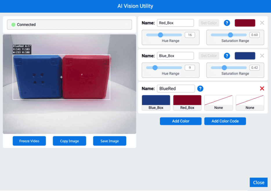 La interfaz de AI Vision Utility muestra un sensor de visión conectado que detecta dos objetos adyacentes, un cuadro azul a la izquierda y un cuadro rojo a la derecha, agrupados en un solo cuadro delimitador blanco etiquetado como BlueRed. La información de detección incluye el ángulo (A:11°), las coordenadas (X:143, Y:103), el ancho (W:233) y la altura (H:108). En el panel derecho, se muestran tres firmas de color: Red_Box, Blue_Box y BlueRed, con rangos de tonalidad y saturación ajustables. La firma BlueRed combina Blue_Box y Red_Box. Debajo de la fuente de vídeo hay botones etiquetados como Congelar vídeo, Copiar imagen, Guardar imagen y Cerrar.