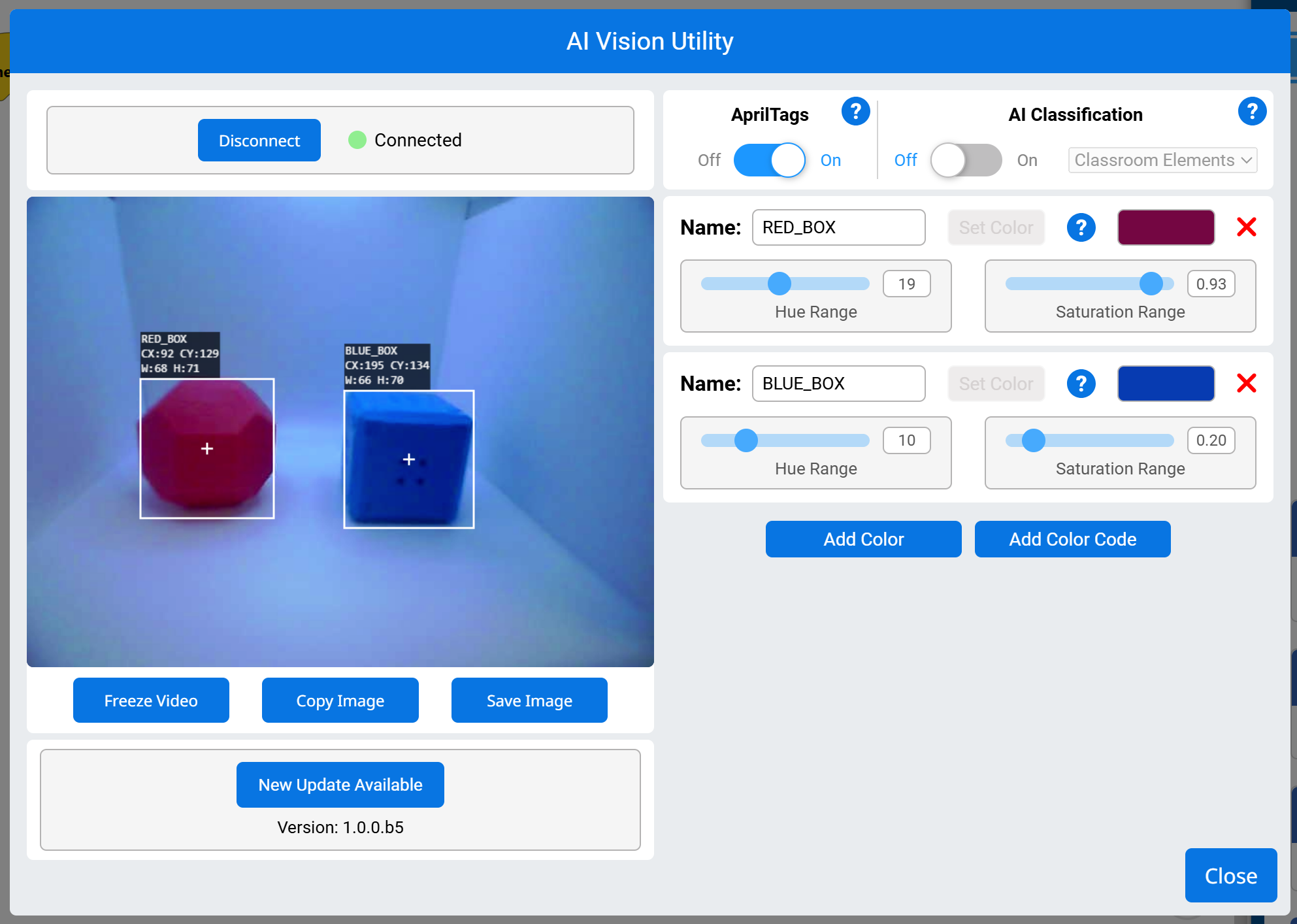 The AI Vision Utility showing a connected vision sensor detecting two colored objects. The left side displays a live camera feed with a blue box on the left and a red box on the right, each outlined with white bounding boxes. Black labels display their respective names, coordinates, and dimensions. The right side contains color signature settings, with sliders for hue and saturation range for both the red and blue boxes. Buttons for adding colors, freezing video, copying, and saving the image are at the bottom, along with a close button in the lower right corner.